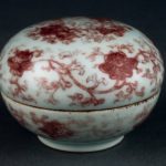 Circular porcelain box with domed cover. There are stylised lotus flowers in underglaze copper red
